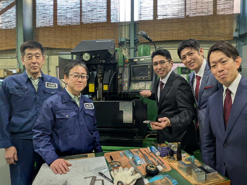 創業の中核メンバーである吉尾氏（右から2人目）は鋼板加工現場の叩き上げであり、「モノづくりの現場で若い世代が生きがいを持って働けるようにしたい」と語る